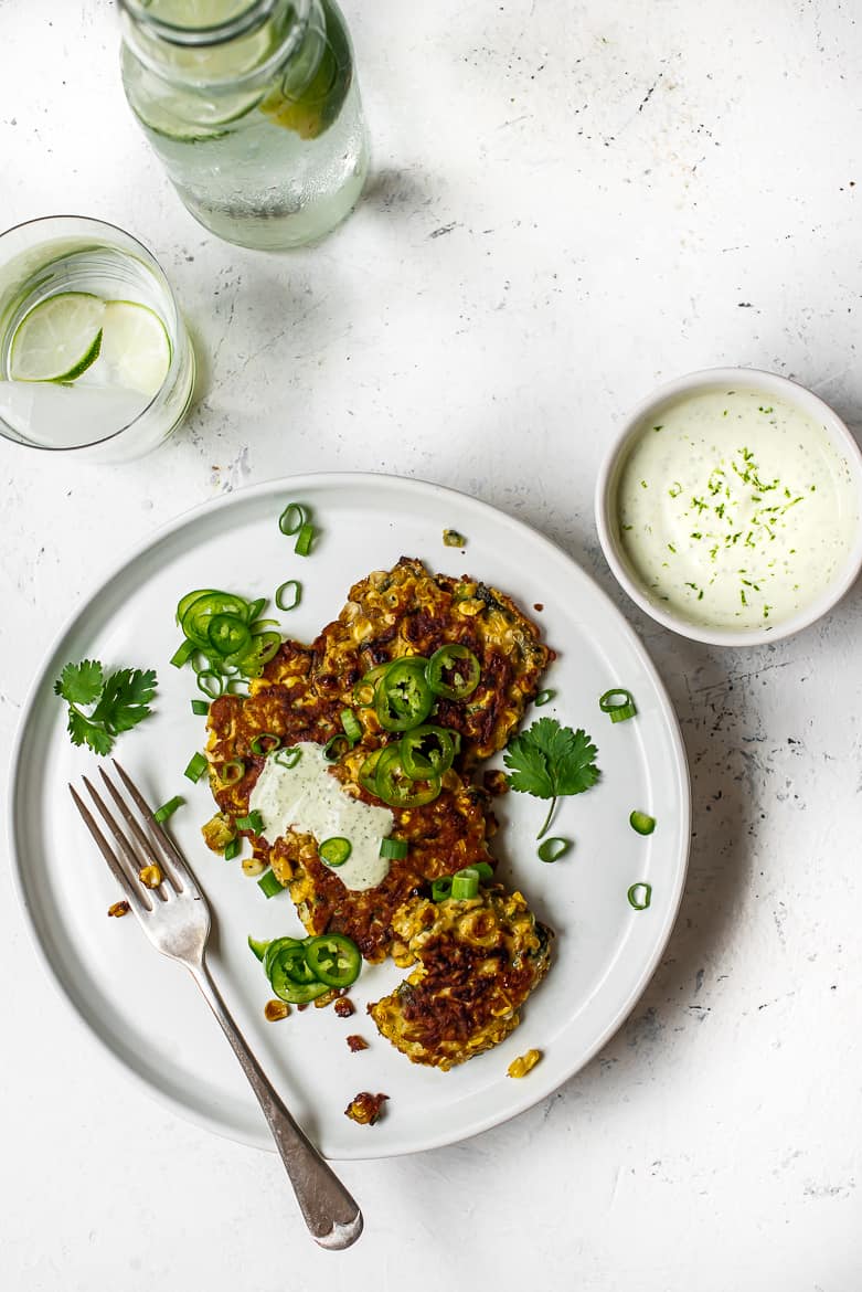 Corn and Poblano fritters on plate with cilantro yogurt sauce and drinks
