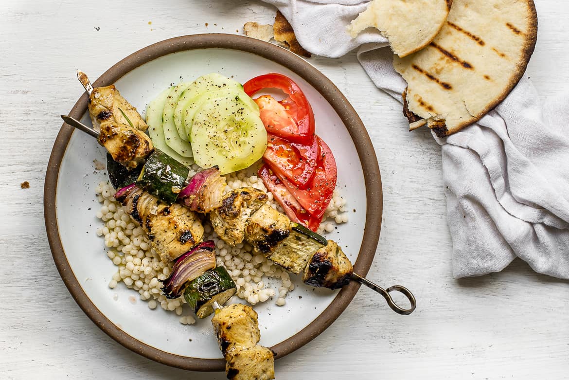 Grilled moroccan chicken skewers on plate with salad and couscous