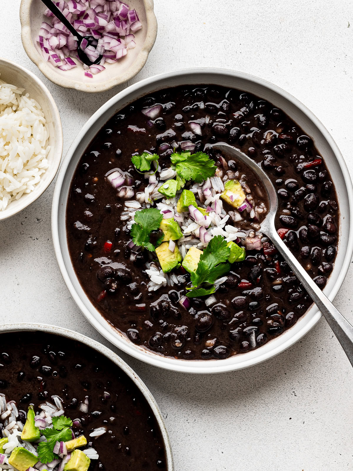 Instant Pot Cuban Black Bean soup served in two white bowls garnished with diced red onion, diced avocado, and white rice