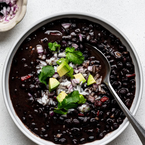 Instant Pot Cuban Black Bean soup served in a white bowl garnished with diced red onion, diced avocado, and white rice