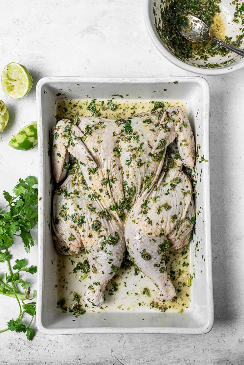 raw spatchcocked chicken marinating with cilantro and lime mixture 