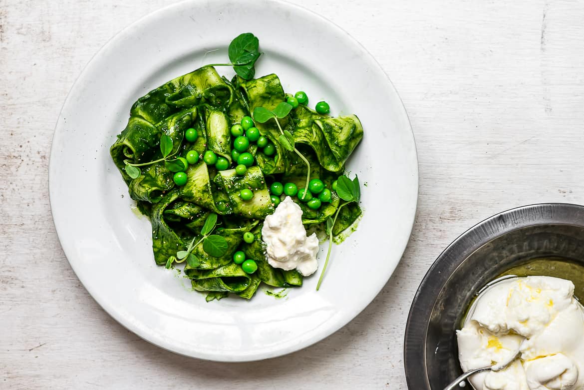 Burrata cheese being topped onto kale sauce pasta with Peas 