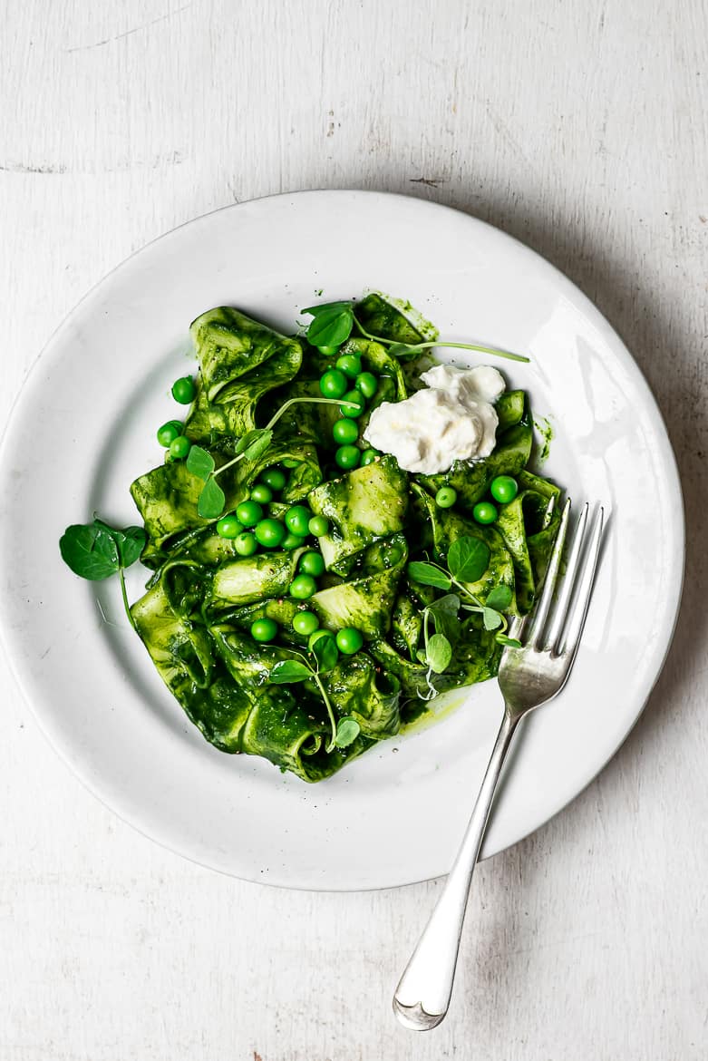 Pappardelle pasta with kale sauce with Peas and Burrata cheese on plate with fork