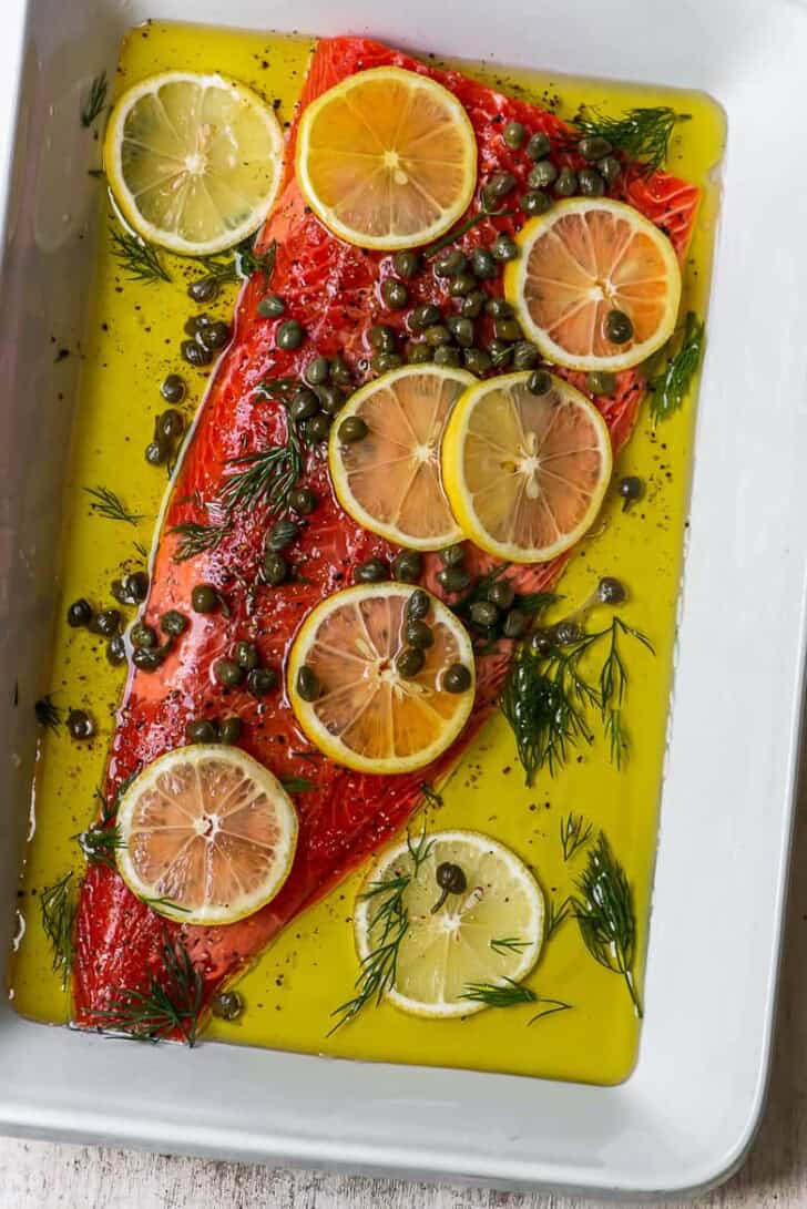 Uncooked Salmon fillet with lemons, capers, dill and olive oil in baking dish