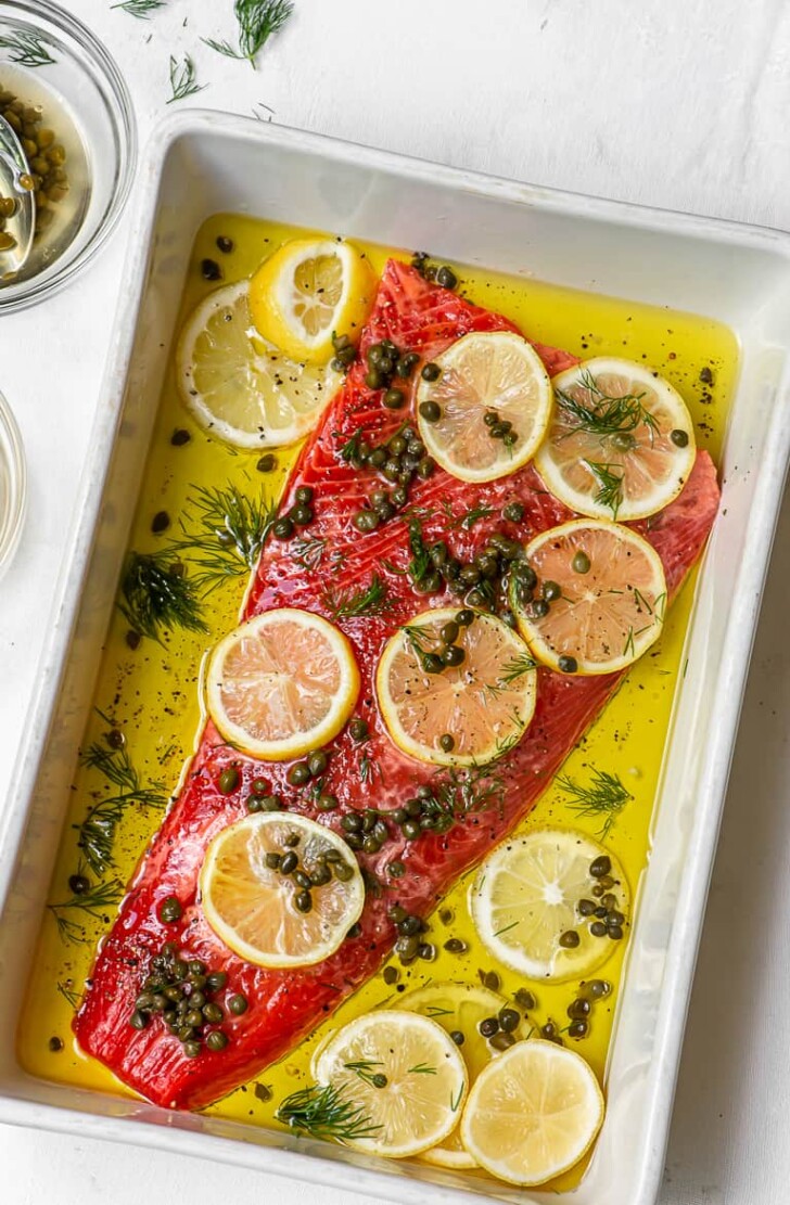 Uncooked Salmon fillet with lemons, capers, dill and olive oil in baking dish