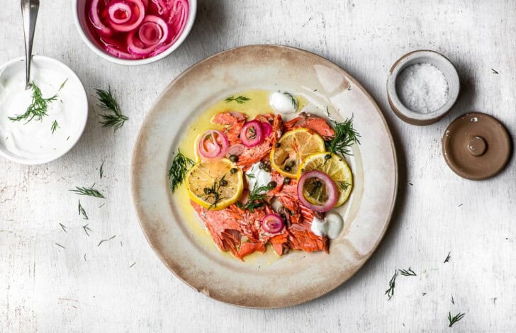 Salmon on plate with pickled onions and yogurt sauce and flaky salt on the side