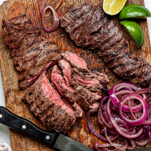 Grilled skirt steak sliced on a cutting board with onions on the side.