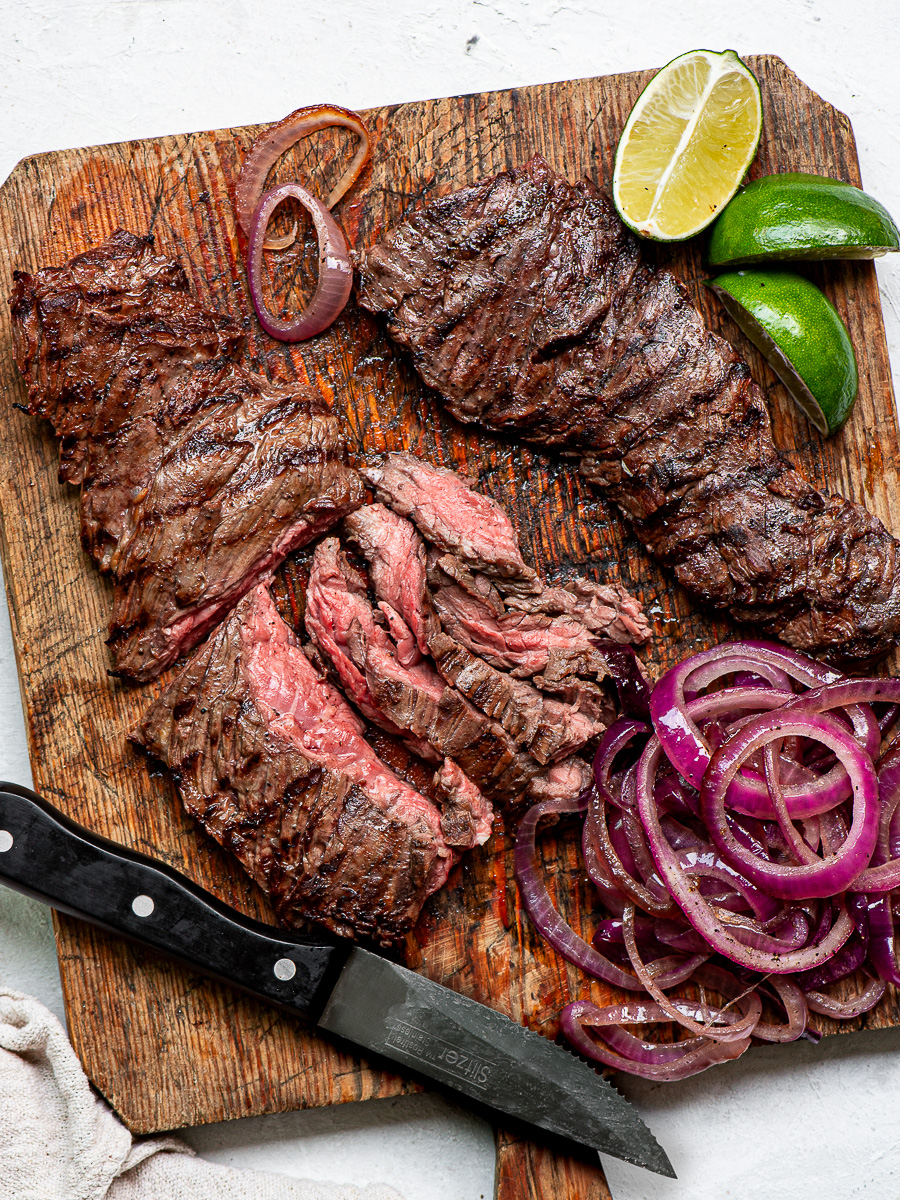 Grilled skirt steak sliced on a cutting board with onions on the side.