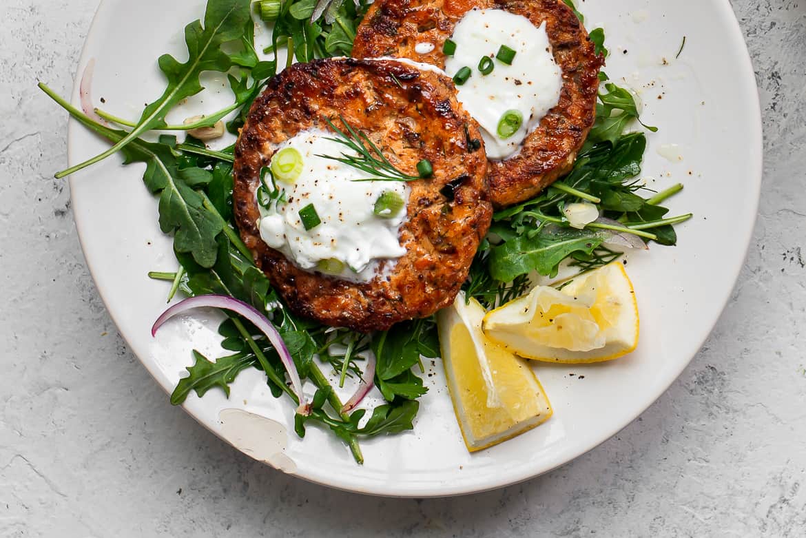 Close up of Salmon cakes on plate with greens and yogurt 