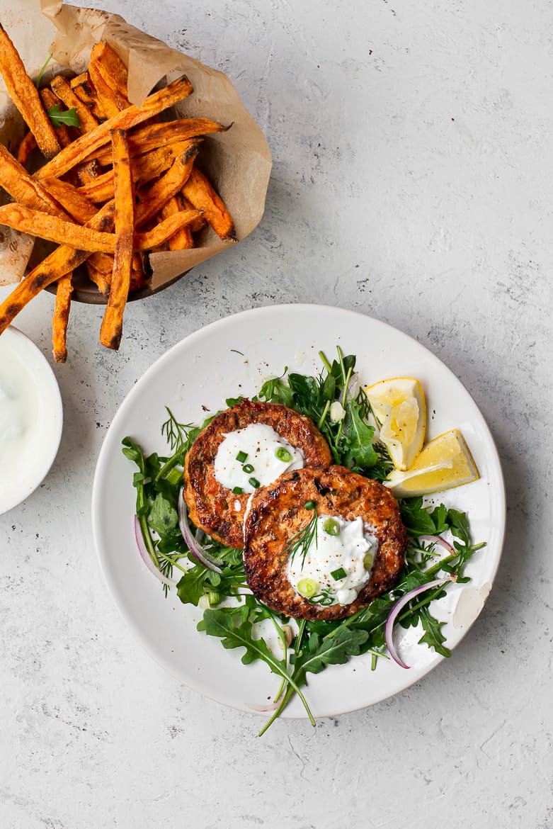 Salmon cakes on plate with greens and yogurt and sweet potato fries