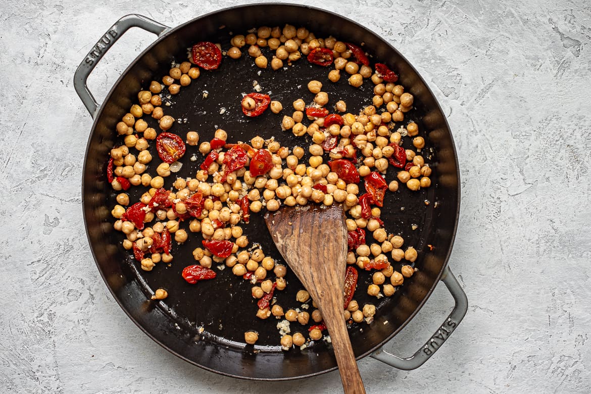Sautéing chickpeas and sun-dried tomatoes in skillet
