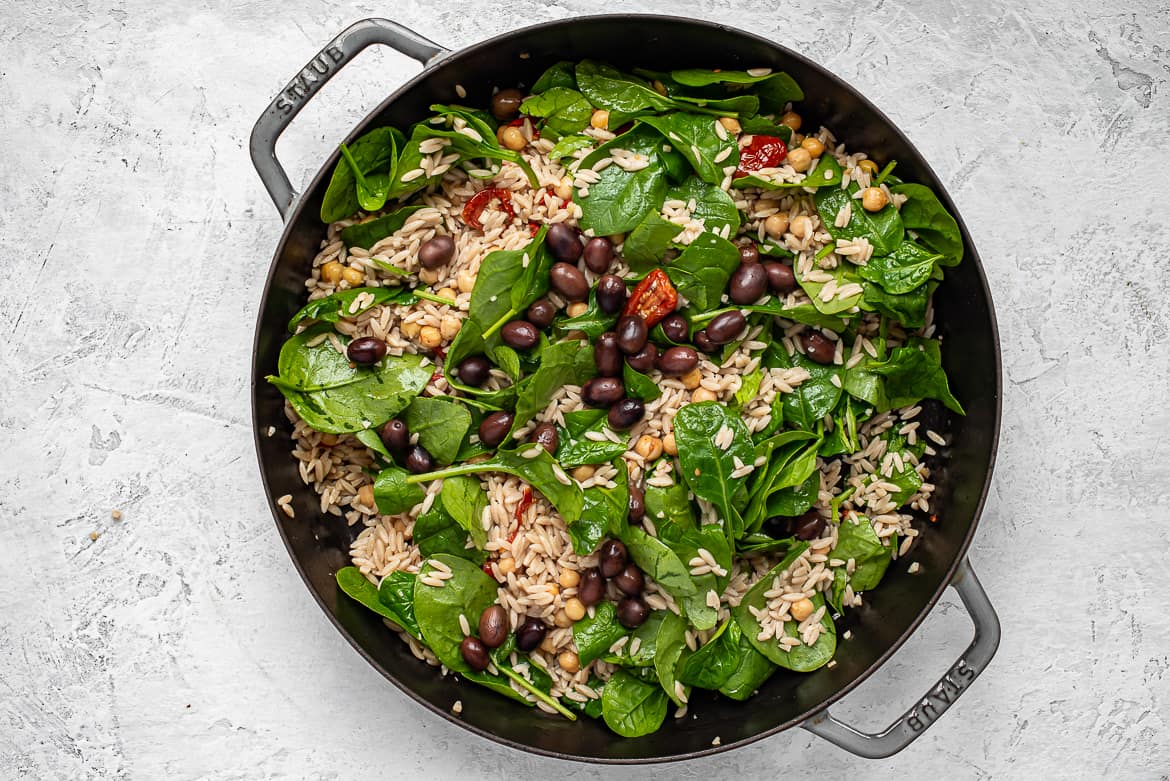 Adding olives to the skillet with orzo, chickpeas and spinach