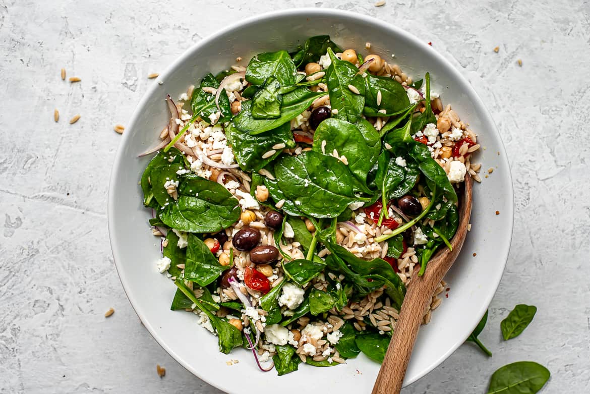 Prepared orzo salad in bowl topped with feta cheese and walnuts