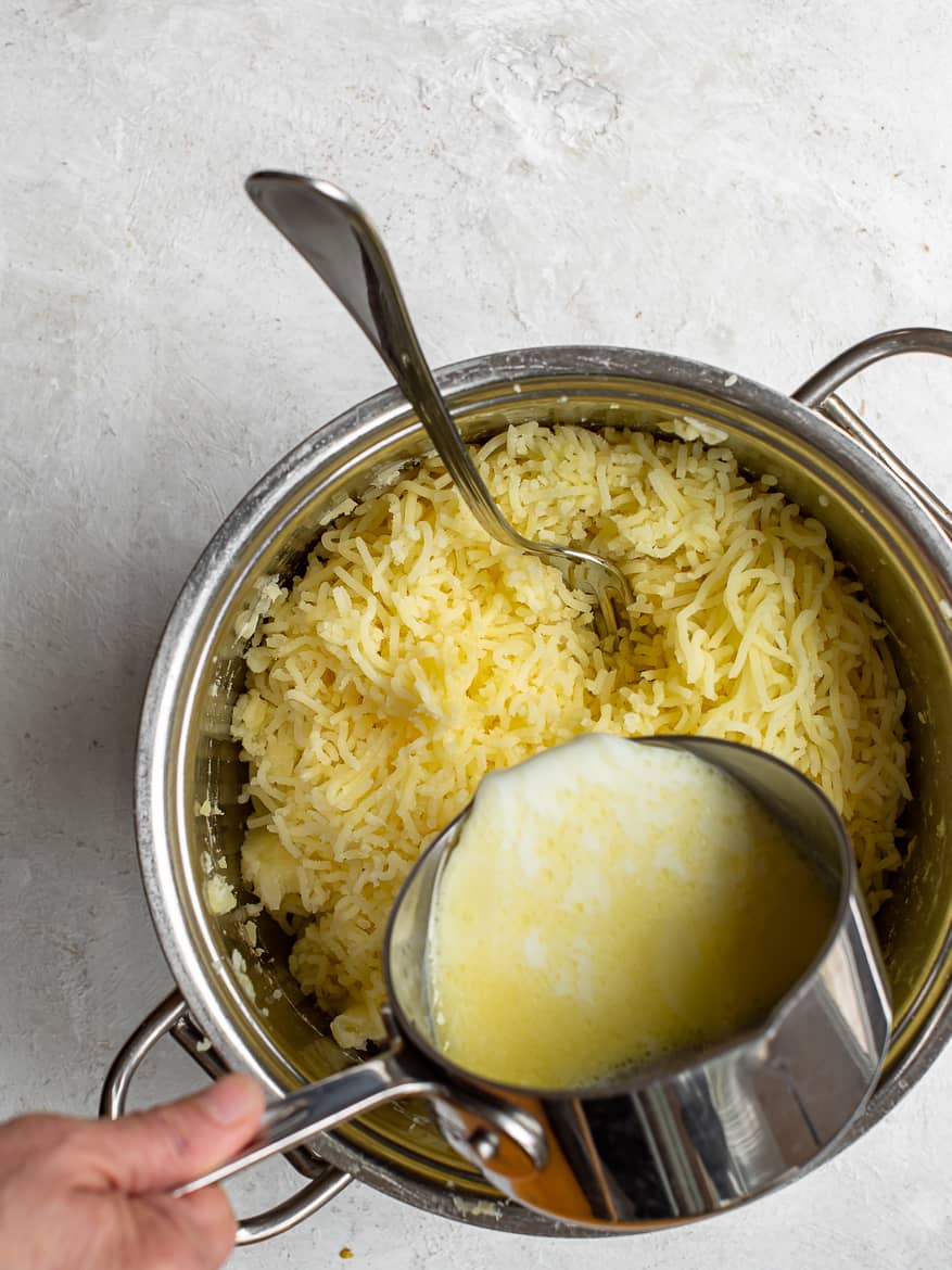 pouring warm milk and butter into potato mash