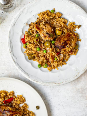 arroz con pollo served on two white plates with salt shaker on the side