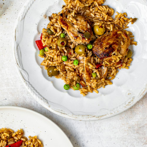 arroz con pollo served on two white plates with salt shaker on the side