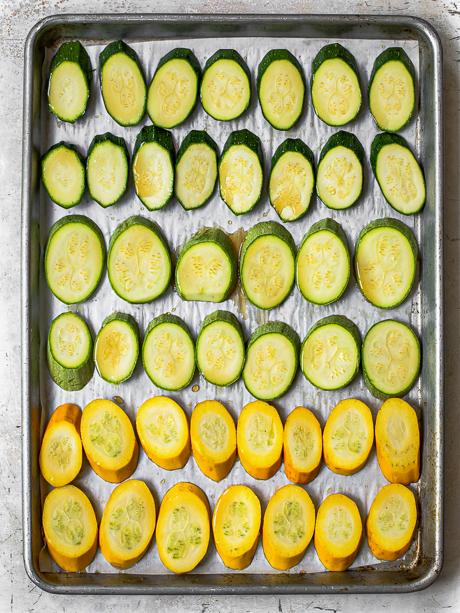Raw zucchini and yellow squash slices laid out in baking sheet ombre-style. 