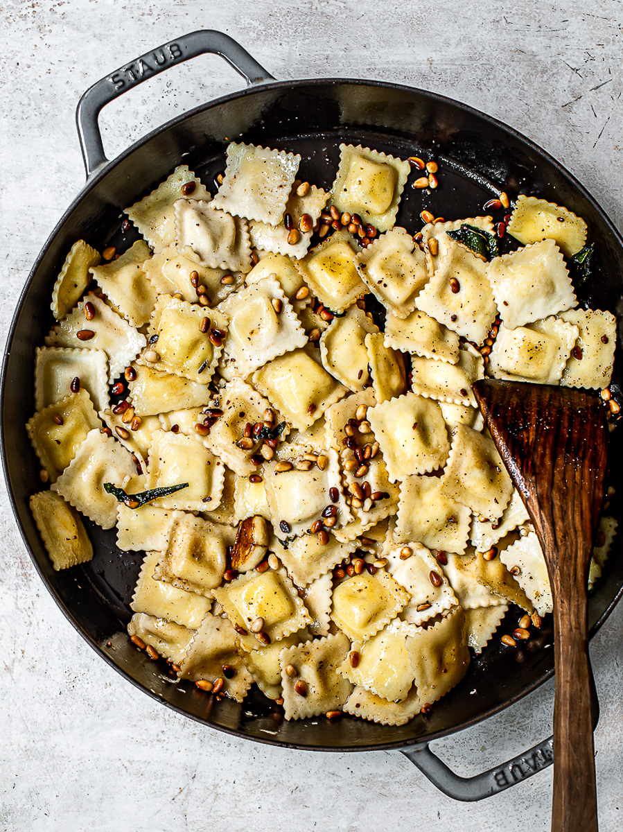 Cooked ravioli pasta sautéed in skillet with pine nuts. 