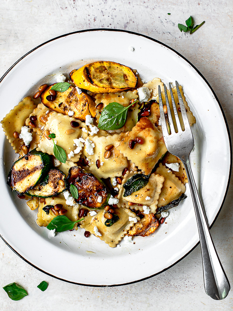 Pasta with summer squash served in white bowl with silver fork. 