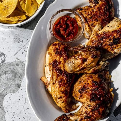 Piri piri chicken on platter with bowl of plantain chips