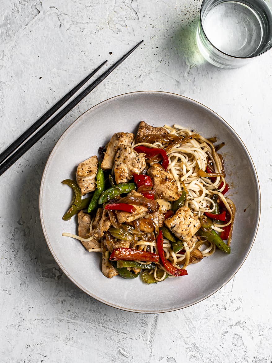 Chicken with green peppers onions and noodles in bowl