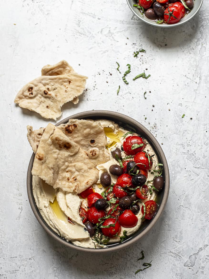 Ultra Smooth Hummus in bowl topped with marinated tomatoes and olives and flatbread