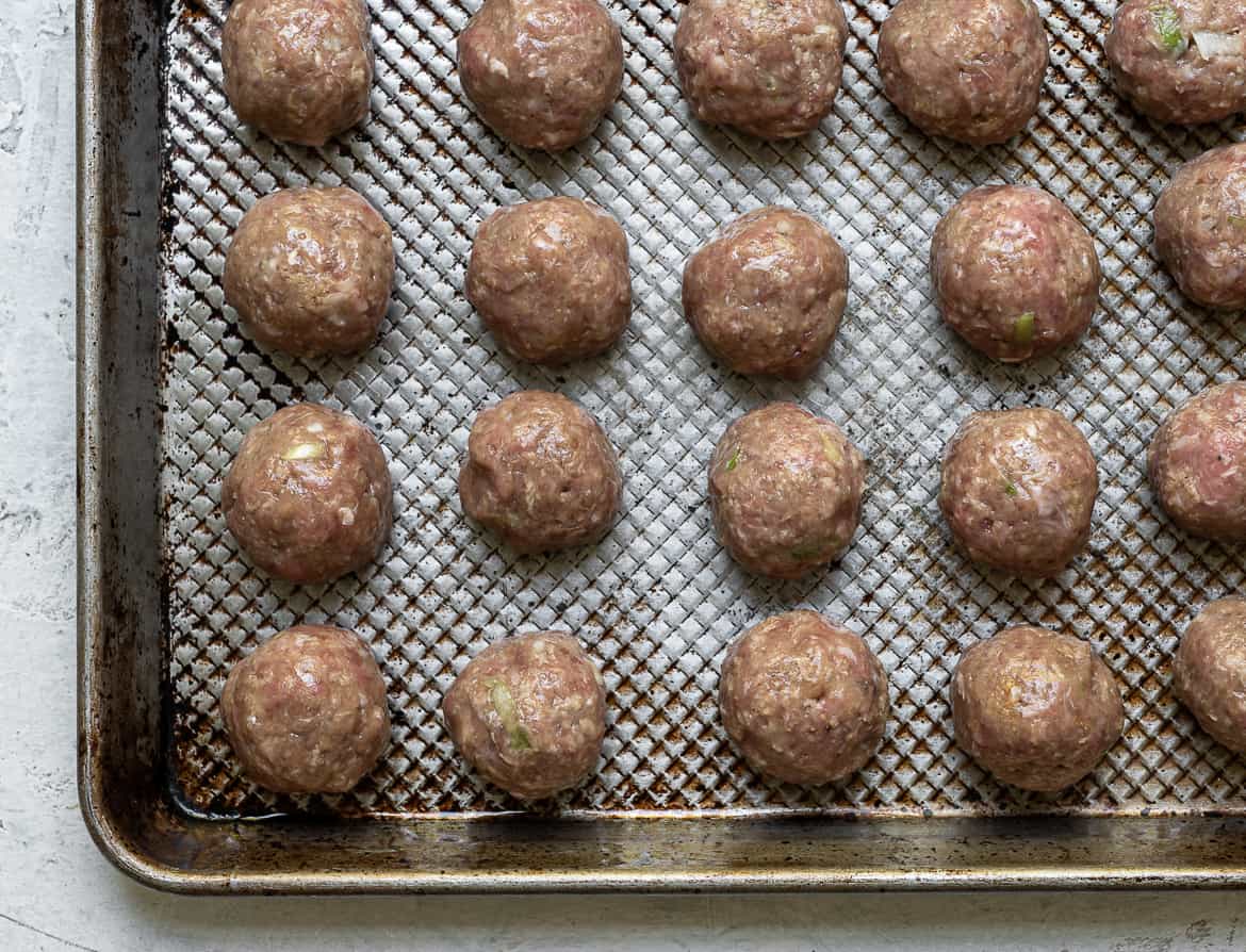 Raw, rolled chicken meatballs on baking sheet