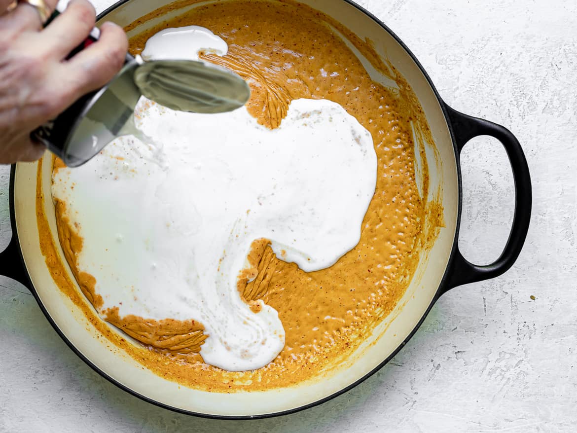 pouring more coconut milk into curry sauce