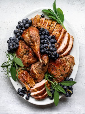 Carved spatchcock turkey on white platter with Concord grapes as garnish