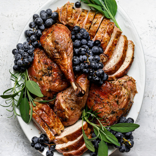 Carved spatchcock turkey on white platter with Concord grapes as garnish.