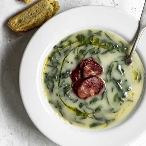 Close up of Caldo verde in soup bowl with chunks of Portuguese corn bread on the side