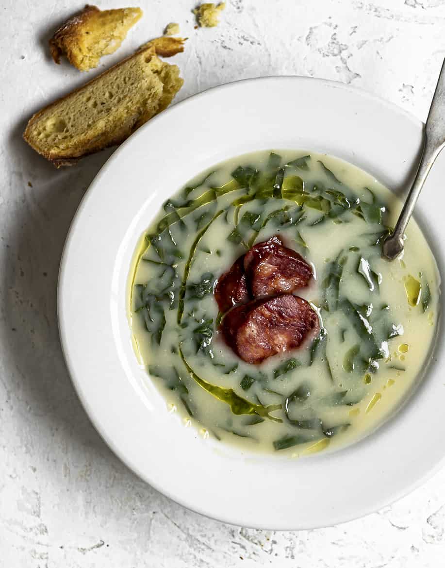 Close up of Caldo verde in soup bowl with chunks of Portuguese corn bread on the side