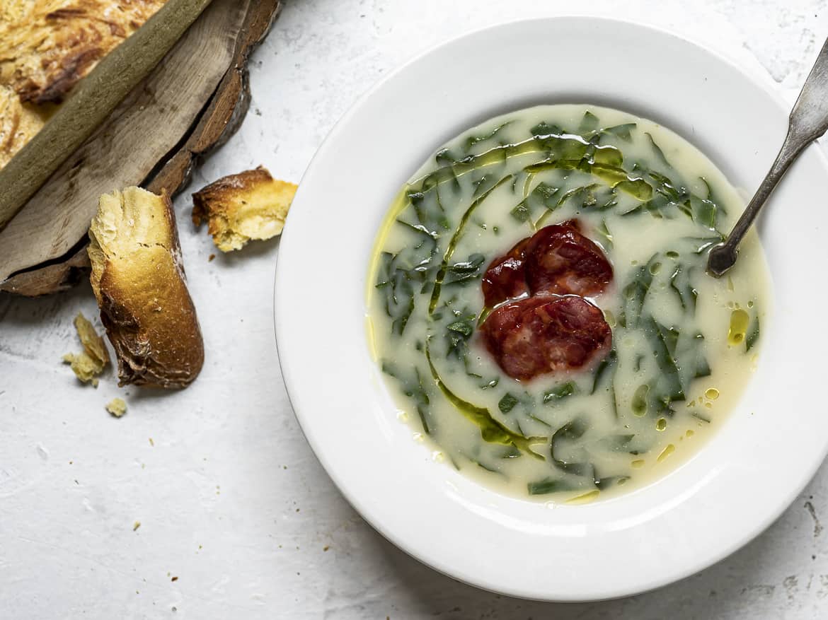 Caldo verde in bowl topped with choriço sausage and bread chunks on the side