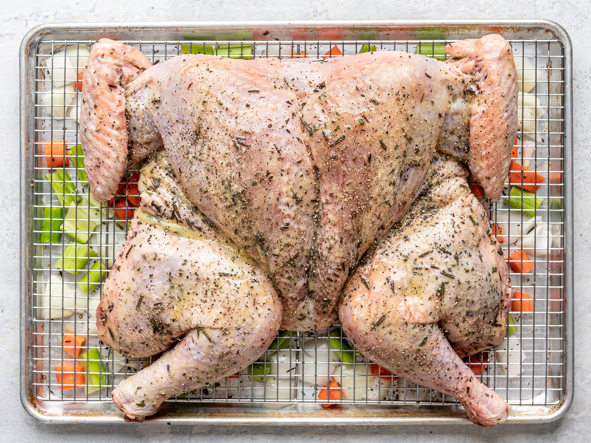 Raw spatchcocked turkey on baking sheet sprinkled with black pepper. 