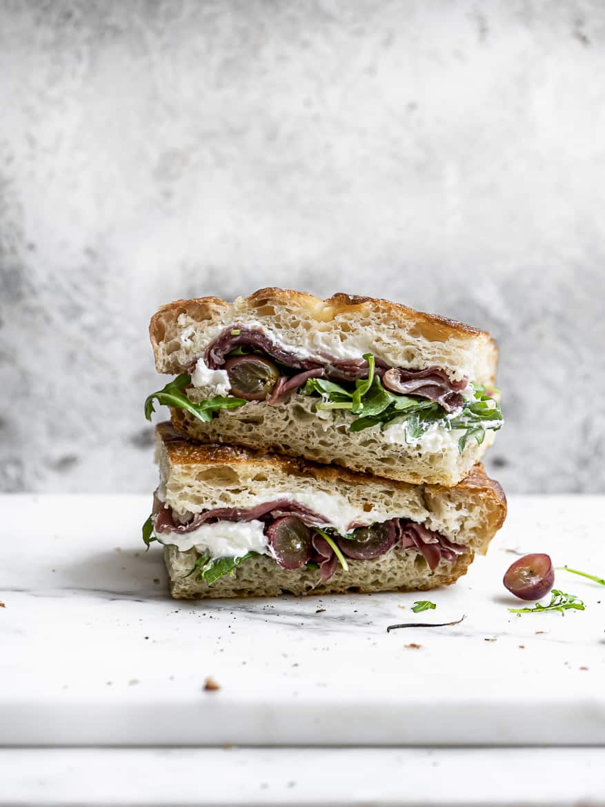 two pieces of grape, arugula, prosciutto and burrata sandwich stacked