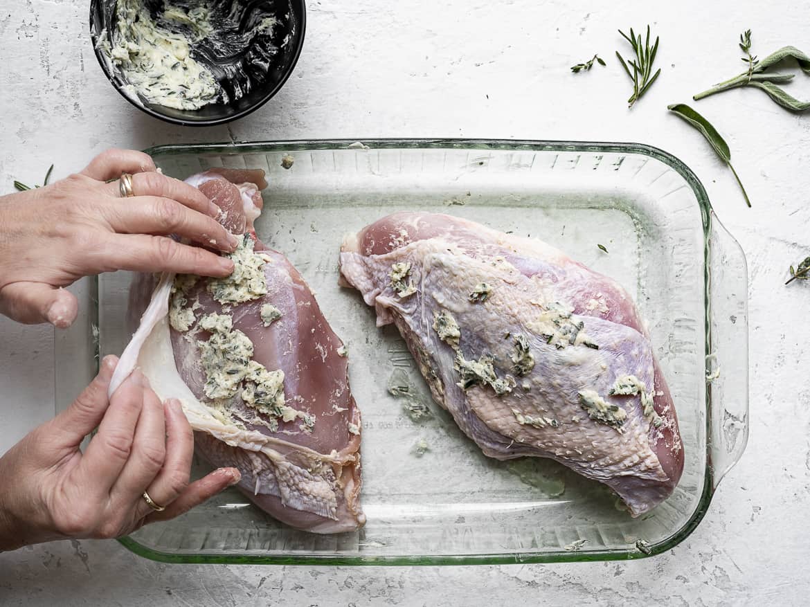 Smearing herb-butter mixture all over turkey breast
