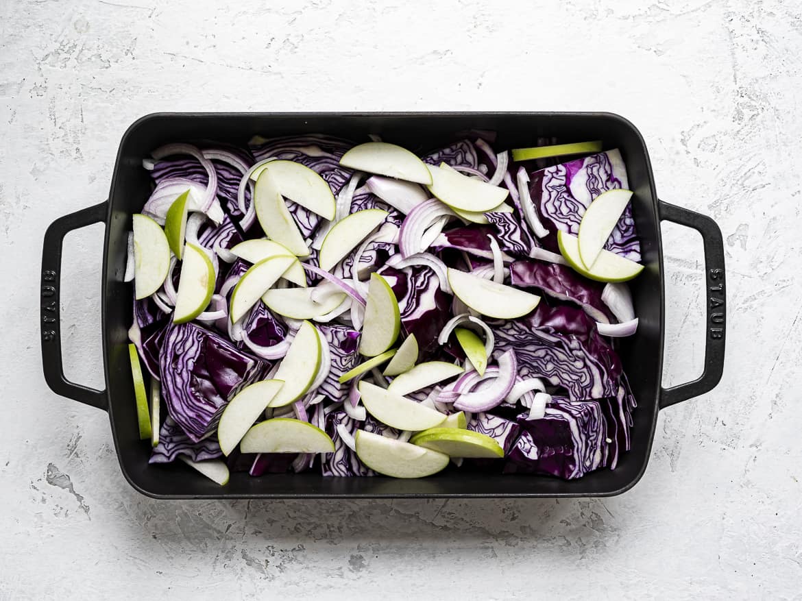 Chopped red cabbage in roasting pan with sliced apples and onions