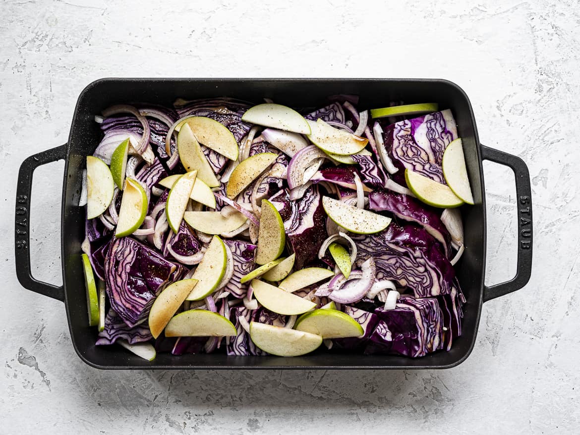 Chopped red cabbage in roasting pan with sliced apples, onions, with spices, apple cider and balsamic vinegar