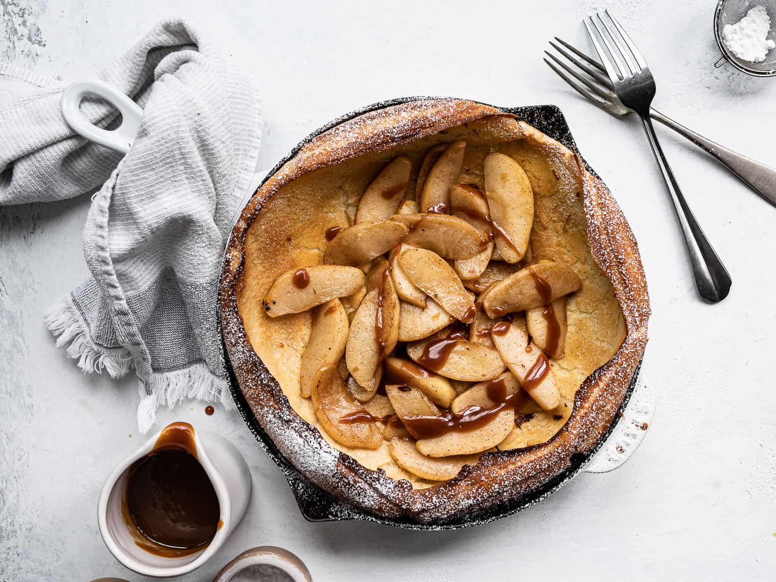 Dutch baby topped with caramelized apples, icing sugar and caramel drizzle