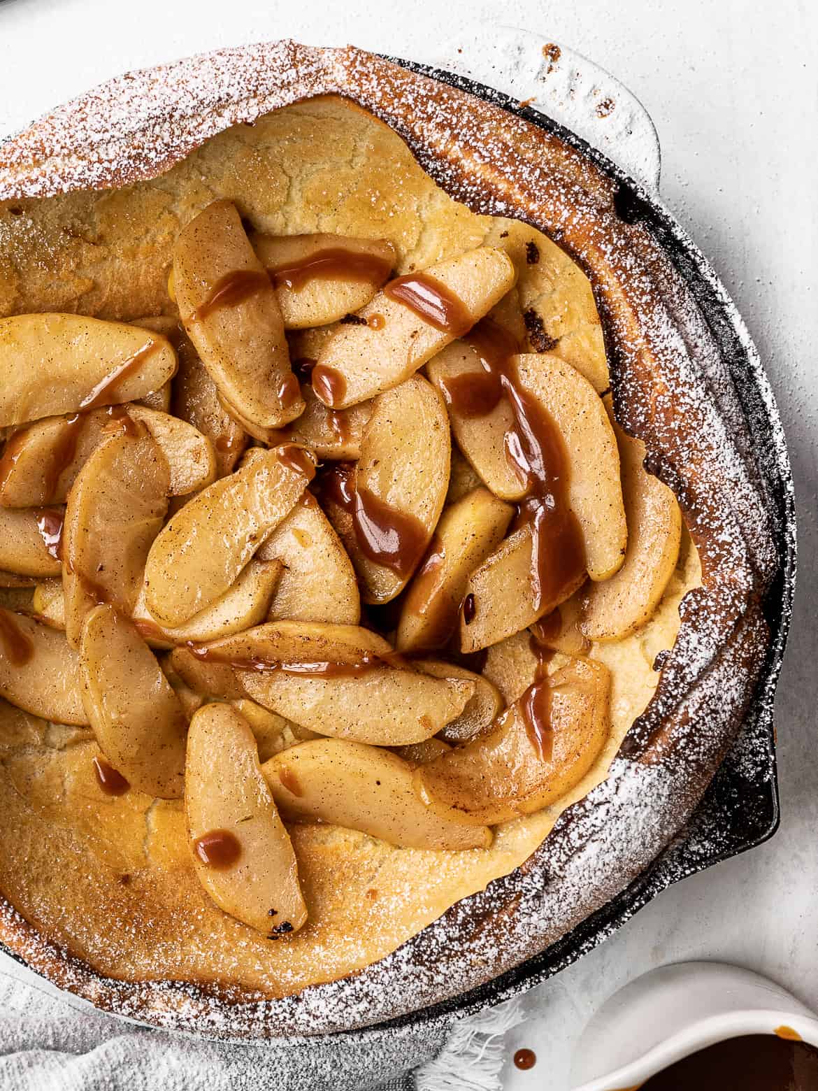 close up of Dutch baby topped with caramelized apples, icing sugar and caramel drizzle