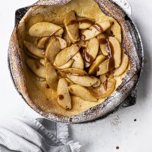 Dutch baby with caramelized apples and drizzle of salted caramel in skillet