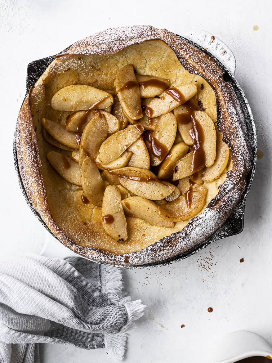 Dutch baby with caramelized apples and drizzle of salted caramel in skillet