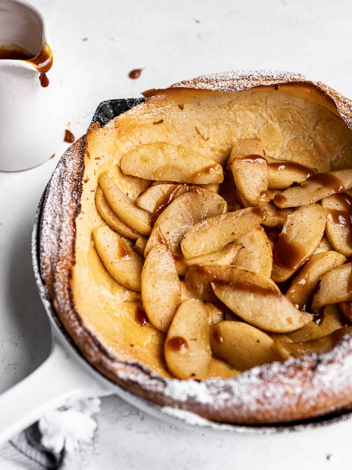 Side view of Dutch baby topped with caramelized apples, icing sugar and caramel drizzle