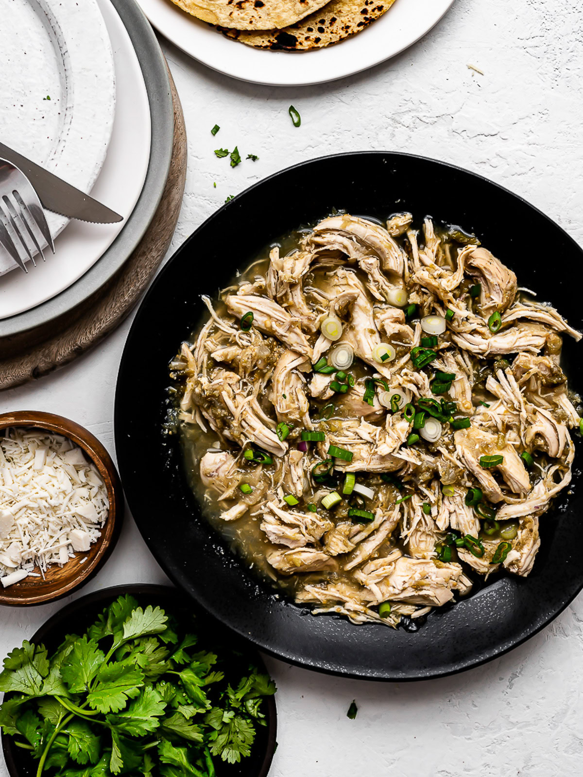 Salsa Verde Chicken in black serving bowl with plates on the side