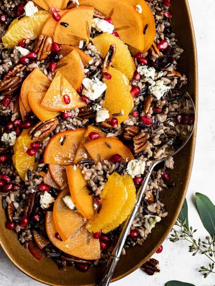 Close up of Mixing wild rice salad with persimmons in served in platter