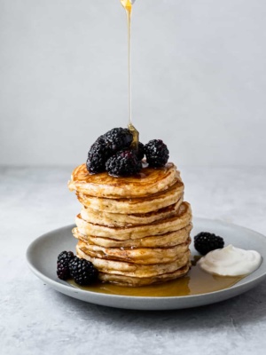 drizzling maple syrup over fluffy yogurt pancake stack