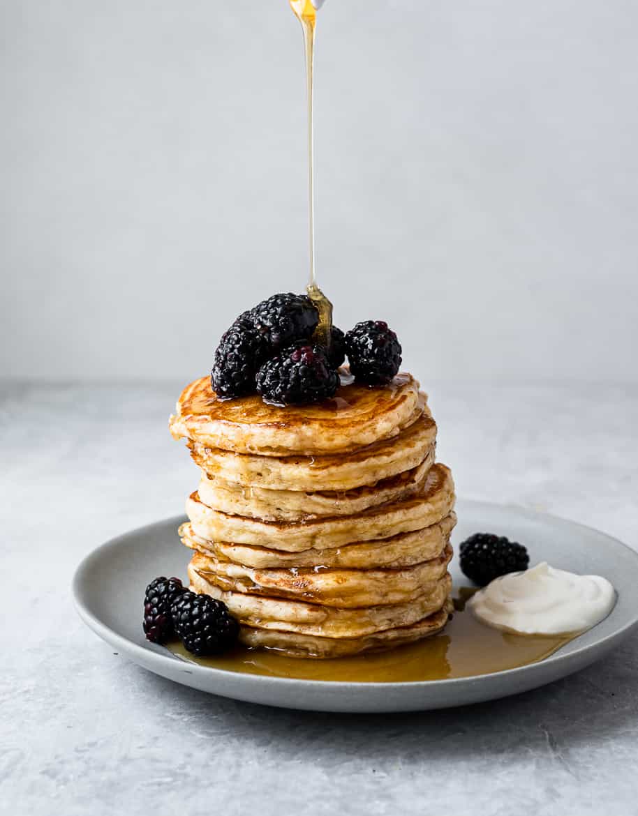 drizzling maple syrup over fluffy yogurt pancake stack