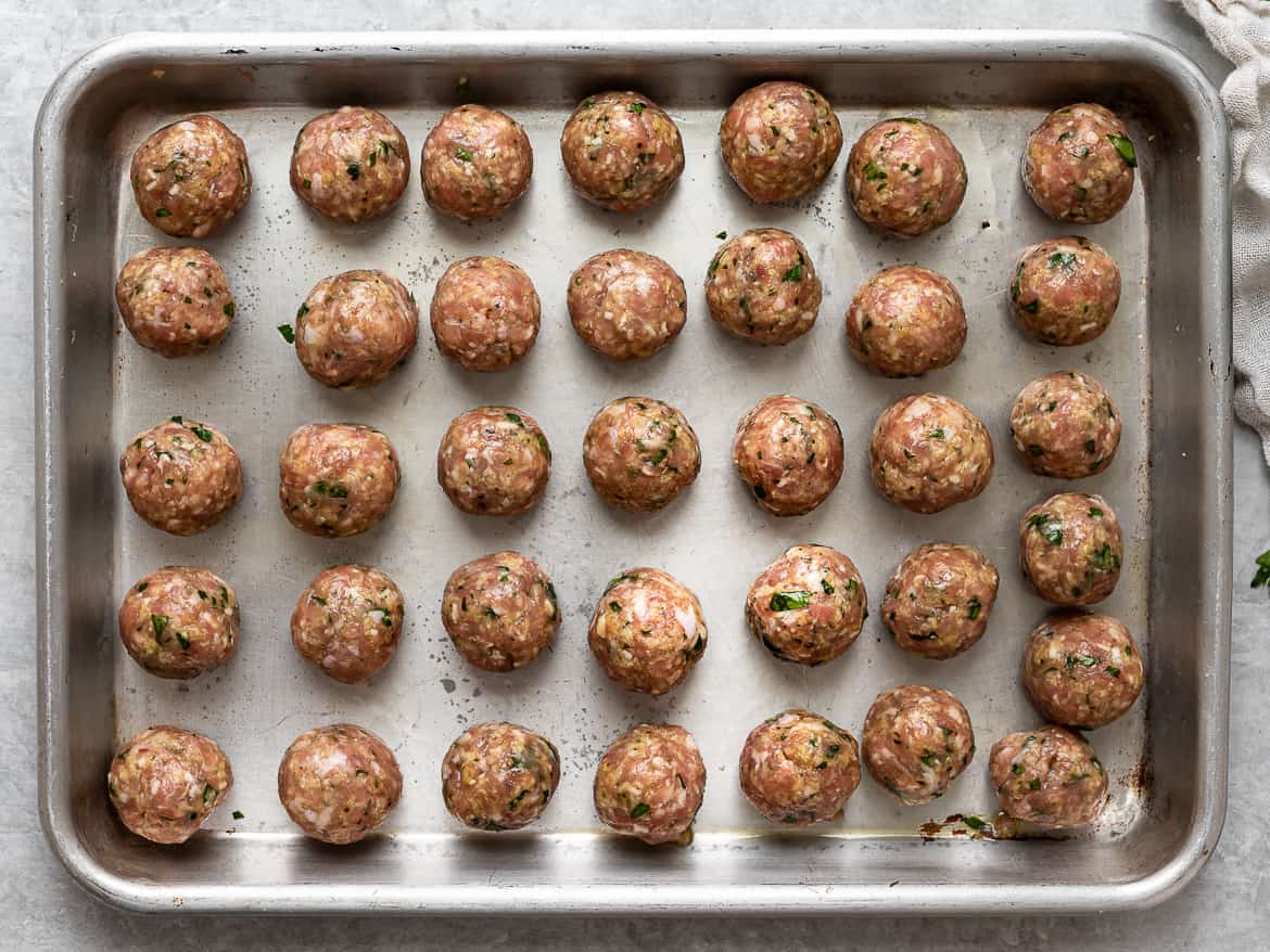 Tiny rolled meatballs on baking sheet.