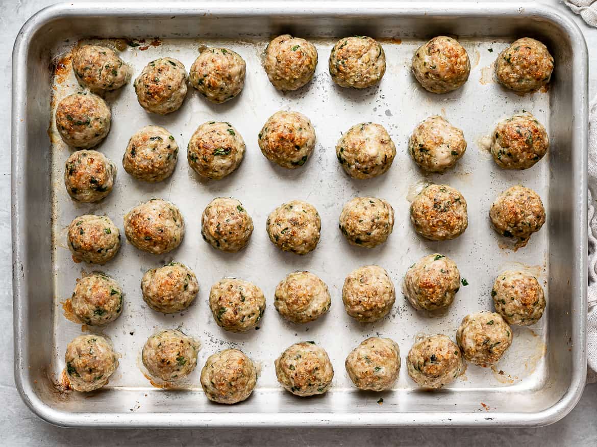 Tiny broiled meatballs on baking sheet.