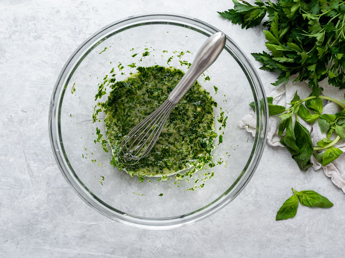 Mixing egg with herbs in large bowl for meatballs.